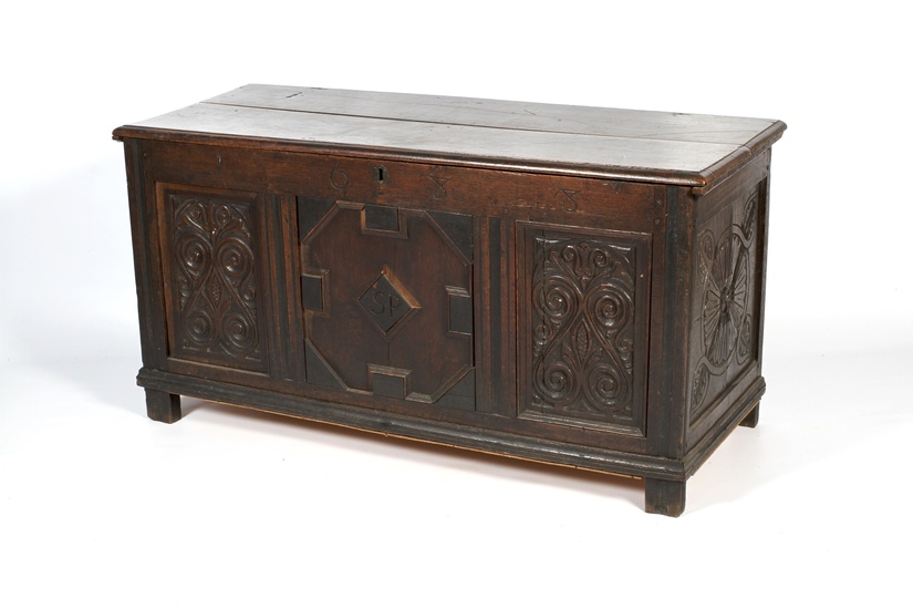 A carved oak coffer. With hinged plank top above panelled...