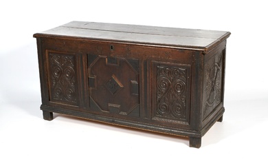 A carved oak coffer. With hinged plank top above panelled...