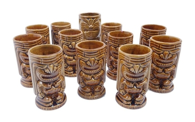 A set of eleven 'Tiki Leilani' brown glazed ceramic drinking tumblers, c.1960, with double sided decoration depicting 'Ku' the god of war, seven inscribed 'USA' to underside, each 13.5cm high, together with one later Tiki tumbler, 15.5cm high (12)
