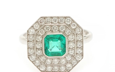 An Art Deco emerald and diamond ring set with an emerald-cut emerald encircled by numerous brilliant-cut diamonds, mounted in platinum. Size 56.
