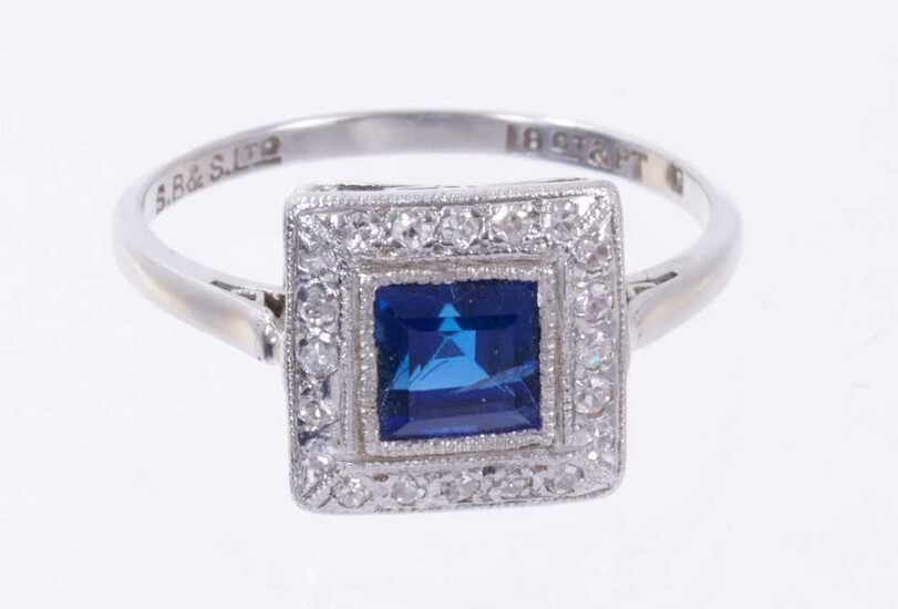 Art Deco style sapphire and diamond cluster ring with a square step cut blue sapphire surrounded by a border of single cut diamonds in platinum millegrain setting on 18ct white gold shank. Ring siz...