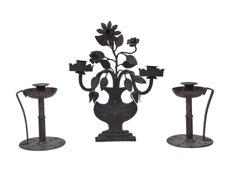 Coberg (German), a pair of Arts and Crafts wrought-iron chamber sticks (lacking match-holders), early 20th Century, stamped 'Coberg', each having a sconce with a bowl shaped drip-pan, on a central column and united to the embellished base by a...