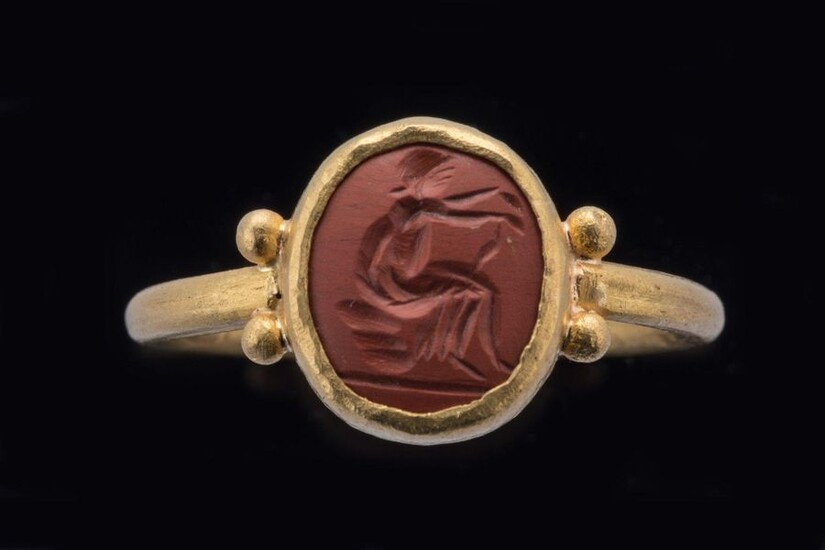 ROMAN INTAIL in red jasper depicting a seated woman. Mounted on a gold ring. Two gold globules adorn the shoulders where the ring attaches to the bezel. 3rd-5th c. A.D. Height intaglio 10, Width 18 mm. Finger circumference: 57. Gross weight : 6 g...