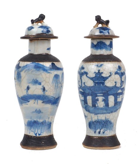 A pair of Chinese porcelain baluster vases and covers, late 19th/early 20th century, painted in underglaze blue with scholars in conversation in a lakeside pavilion, with moulded foo dog finials to the covers, four-character incised marks to bases...
