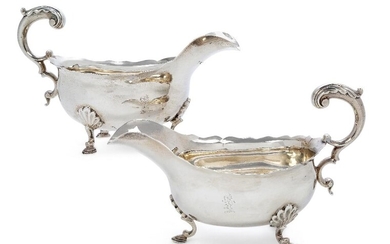 A pair of George III silver sauceboats, London 1797 and 1798, Peter & Ann Bateman, both raised on three shell-shouldered pad feet, the double scroll handles to scalloped rims, engraved with lion rampant crests to bodies, 18.5cm long, 11.5cm high...