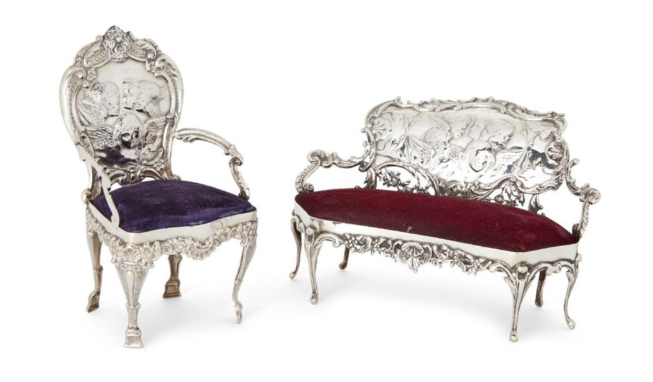 Two Edwardian novelty silver pincushions, London, 1902, William Comyns, designed as a sofa and chair, both with velvet seat pincushions and putti-decorated chair backs, chair 14.2cm high, sofa 9.6cm high (2)