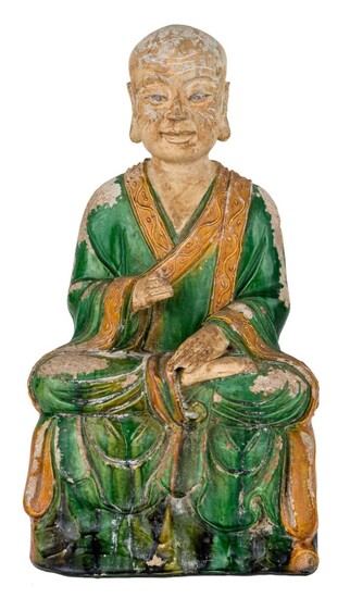 A large Chinese fahua-glazed stoneware figure of a monk, Ming dynasty, seated on a square throne in ardha padmasana with right hand raised, head tilted downwards, wearing a voluminous robe covered in green glaze with yellow border decorated in...