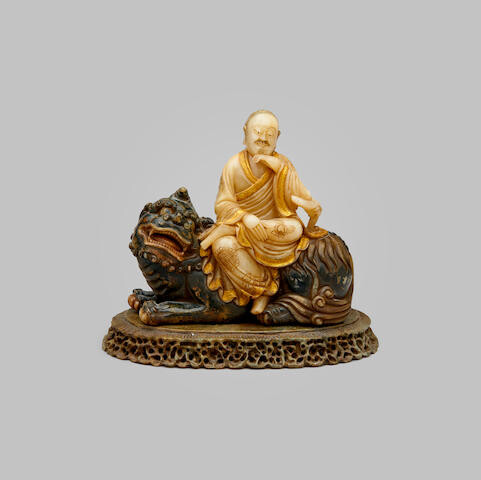 A tinted and parcel-gilt soapstone figure of an arhat seated on a qilin
