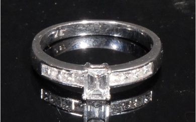 An 18ct white gold diamond ring, the central emerald cut sto...
