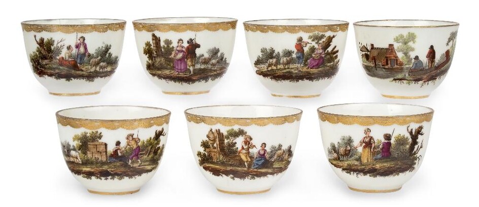 Seven Amstel porcelain teabowls, c.1785, blue script marks and incised marks, painted with pastoral vignettes with figures at various pursuits in landscapes with trees, monuments, buildings, livestock and ruins below elaborate gilt borders, the...