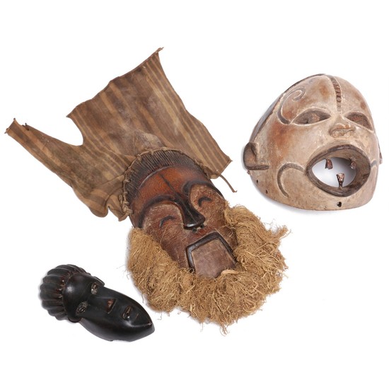 Three masks of carved patinated wood, one mounted with raffia and cloth, traces of black and white pigment. Bassa, Igbo and D. R. Congo style. H. 19–32 cm. (3)