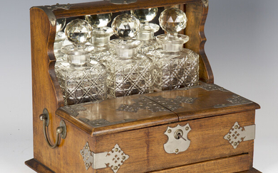 An Edwardian oak and plate mounted three-bottle tantalus, the double-hinged compartment above a draw