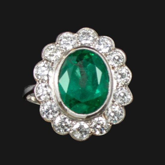 An emerald and diamond cluster ring, centred with an oval-shaped...