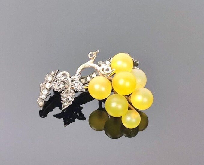 Brooch in yellow and white gold simulating a vine branch holding a bunch of grapes in tinted glass. The vine is decorated with small diamonds.