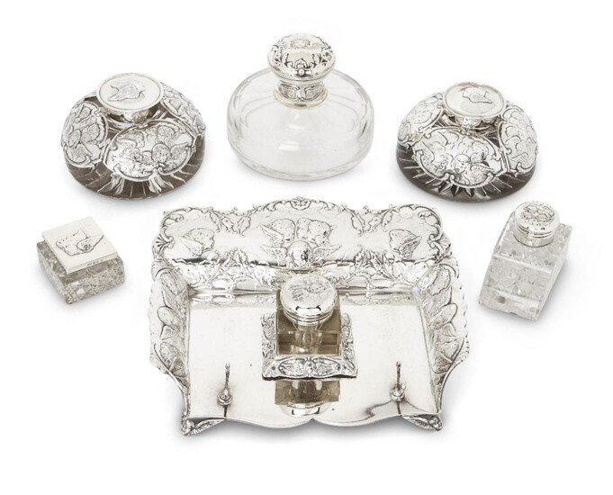 Six various putti-decorated silver mounted inkwells, including one with silver inkstand, the group comprising: a silver mounted glass inkwell (London, 1903, William Comyns & Sons) on shaped rectangular inkstand, London, 1896, William Comyns & Sons...