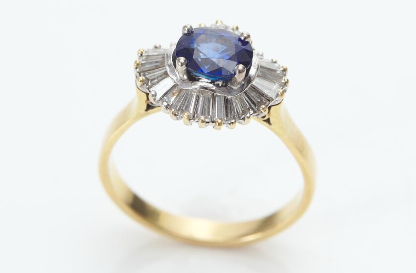 A SAPPHIRE AND DIAMOND RING IN TWO TONE 18CT GOLD, THE OVAL CUT BLUE SAPPHIRE ESTIMATED 1.67CTS, WITHIN A SURROUND OF TAPERED BAGUET...