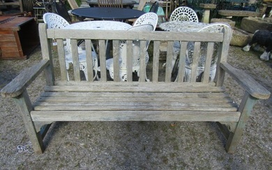 A weathered teak garden bench with slatted seat and back, wi...