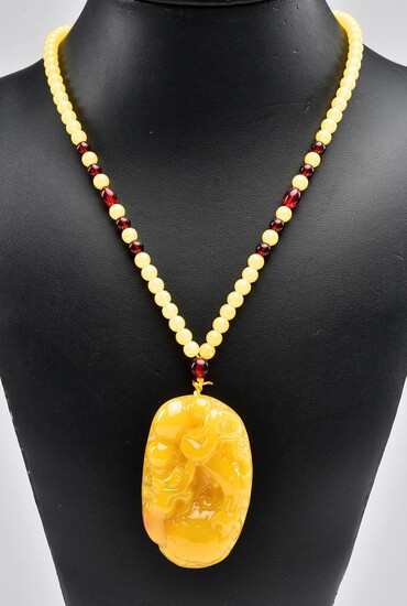 A RECONSTITUTED CARVED AMBER PENDANT NECKLACE