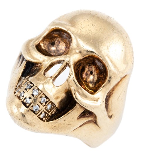 A 9CT GOLD DIAMOND SKULL RING; 30.7 x 22.3mm skull with 10 round brilliant cut diamond set teeth, size X, wt. 20g.