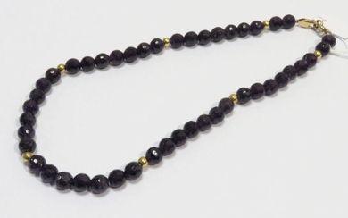 Collier de perles d'améthystes facettées de 10mm environ, intercallées par sept boules en or jaune de 5mm environ. Poids brut : 67g. Long : 52 cm.