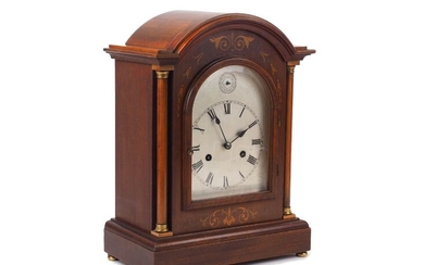 An early 20th century mahogany inlaid bracket clock, glazed door enclosing silvered dial and black Roman numerals, turned columns to each side, the back door enclosing brass movement and a gong orchestra, plinth base Please note that Roseberys do...