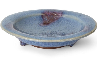 A Chinese Jun-type glazed dish, late Qing Dynasty/Republic, the shallow vessel with a flat, everted rim, the dark stoneware biscuit covered overall in a thick, glassy glaze stopping short of the foot, 12.7cm diam. 清晚期/民國 仿鈞釉三足盤