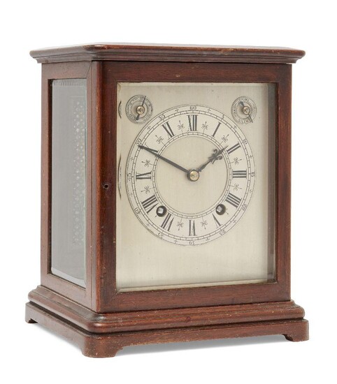 A German mahogany cased four glass mantel clock, early 20th century, the mahogany case with moulded cornice over bevelled glass panels, with pierced quatrefoil brass panel to reverse, on plinth base and bracket feet, the silvered square dial with...